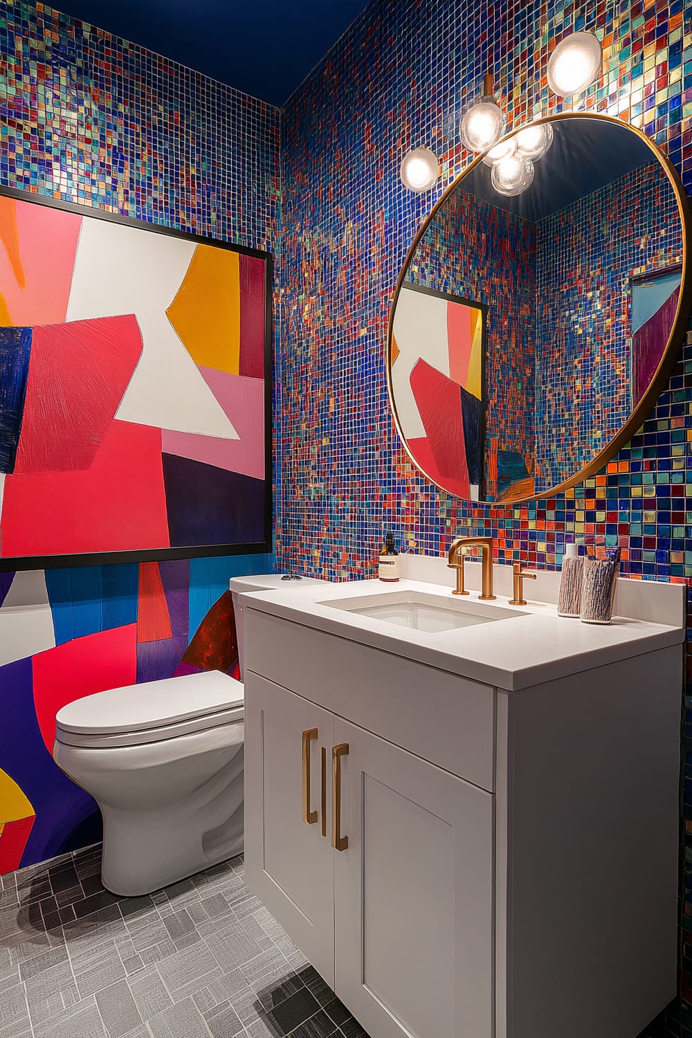 A vibrant bathroom with a mix of vivid colors and modern fixtures. Walls are adorned with small, multicolored mosaic tiles, creating a dynamic, lively atmosphere. A large, abstract, colorful painting featuring bold shapes and contrasting hues is mounted above the toilet. The vanity has a white countertop, golden brass faucets, matching hardware, and a round mirror with an elegant golden frame. Lighting above the mirror consists of three modern, round bulbs.