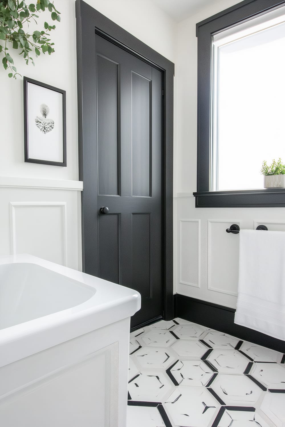 A bathroom features a white bathtub, a black door with matte finish, and a window with black trim. The floor showcases hexagonal white tiles with black patterns. The walls have white wainscoting, adorned with a black-framed picture and a black towel rod holding a white towel. A green plant in a pot adds a touch of nature in the corner by the window.