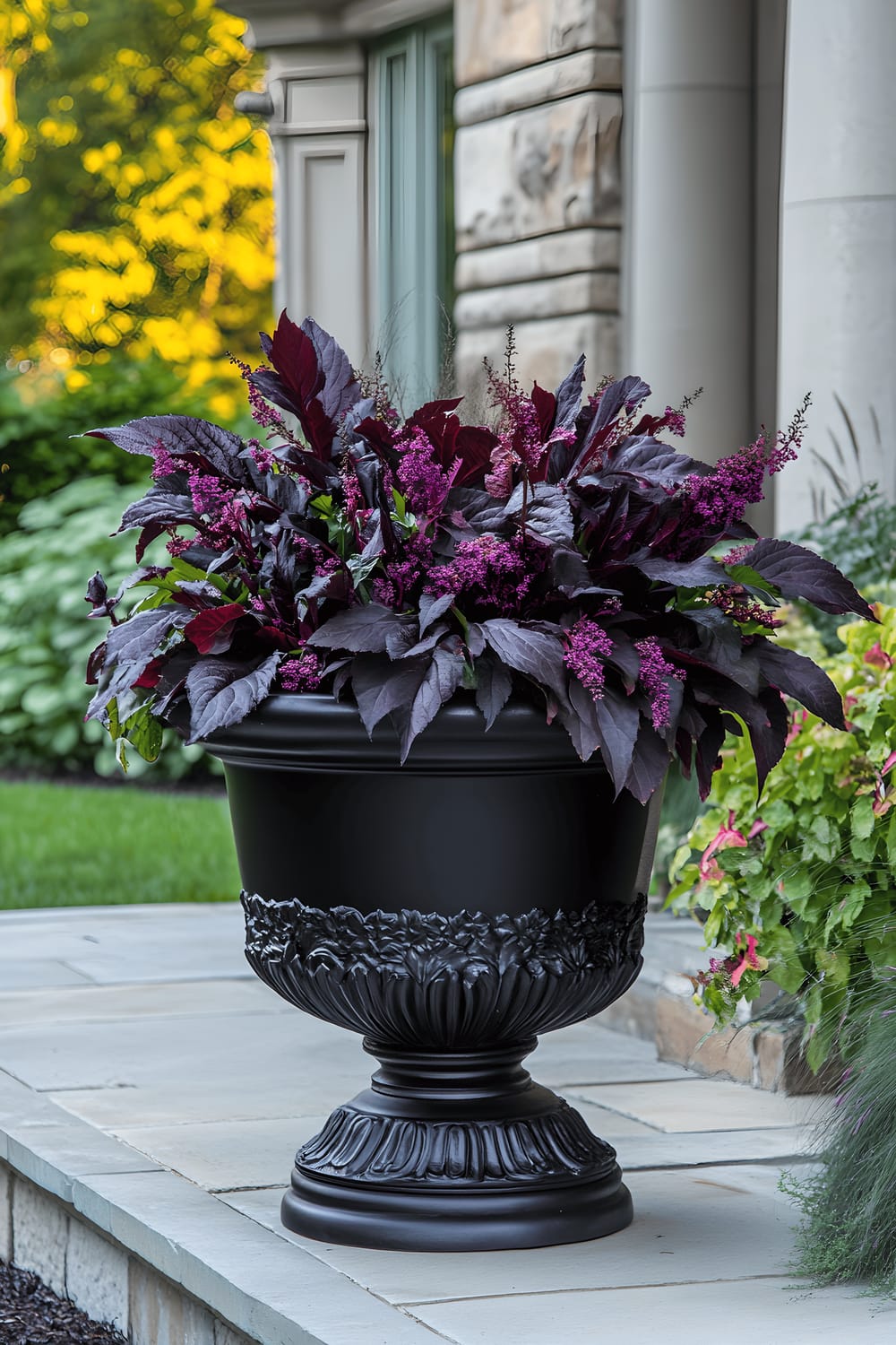 A large black cast-iron urn planter brims with dark-hued plants like Black Mondo Grass, Dark Opal Basil, Persian Shield, and Chocolate Cosmos. The urn stands majestically on a mottled stone patio, its dramatic presence highlighted in the fading twilight illuminating the scene.