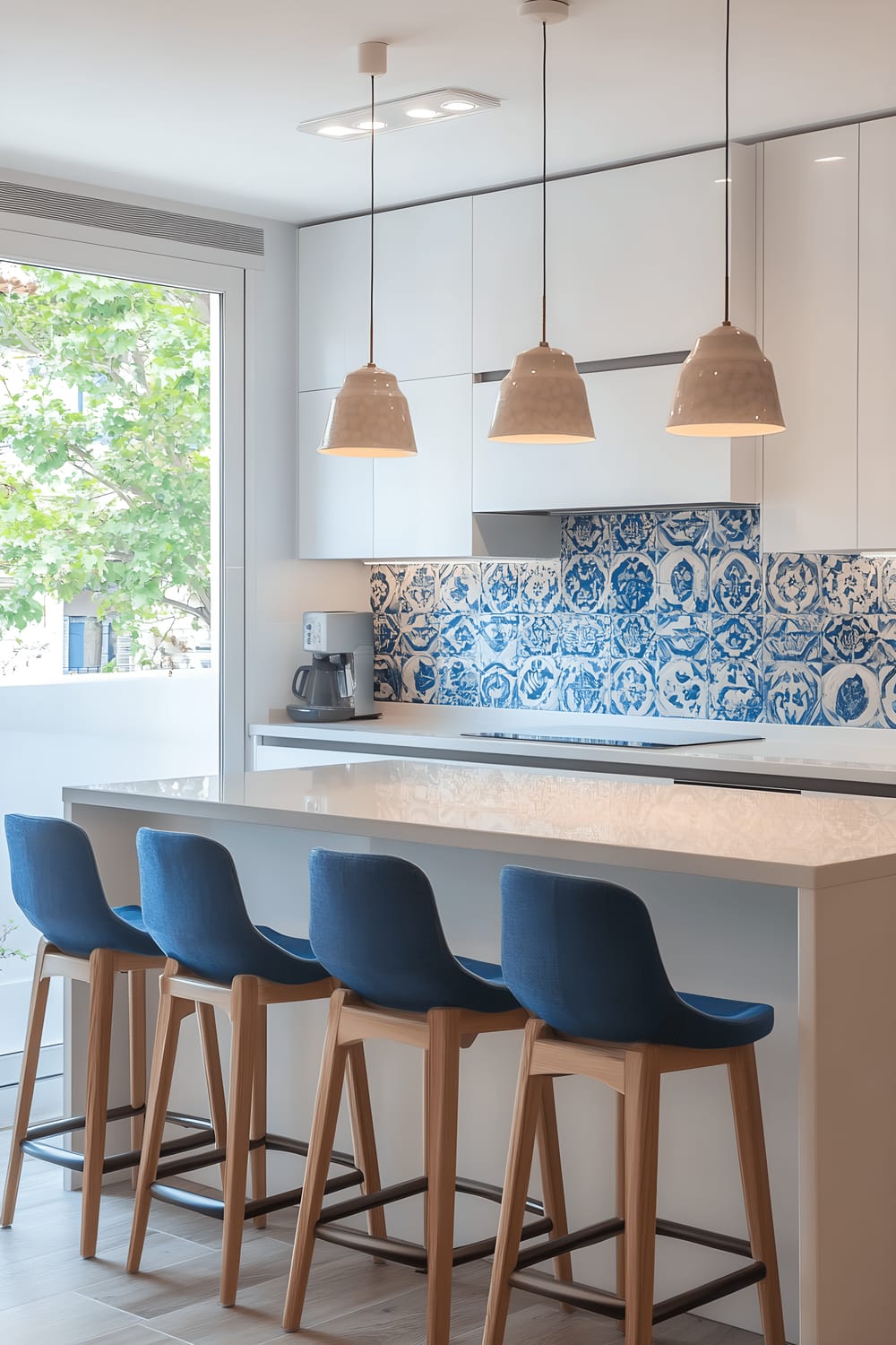 A contemporary kitchen showcasing a harmonious blend of modern and traditional elements, with minimalist white cabinetry, stainless steel appliances, and a vibrant blue and white Barcelona ceramic tile backsplash. The room is centered around an island with bar stools, which are upholstered with Catalan-inspired fabrics. The kitchen is amply lit by a large window letting in streams of natural light.