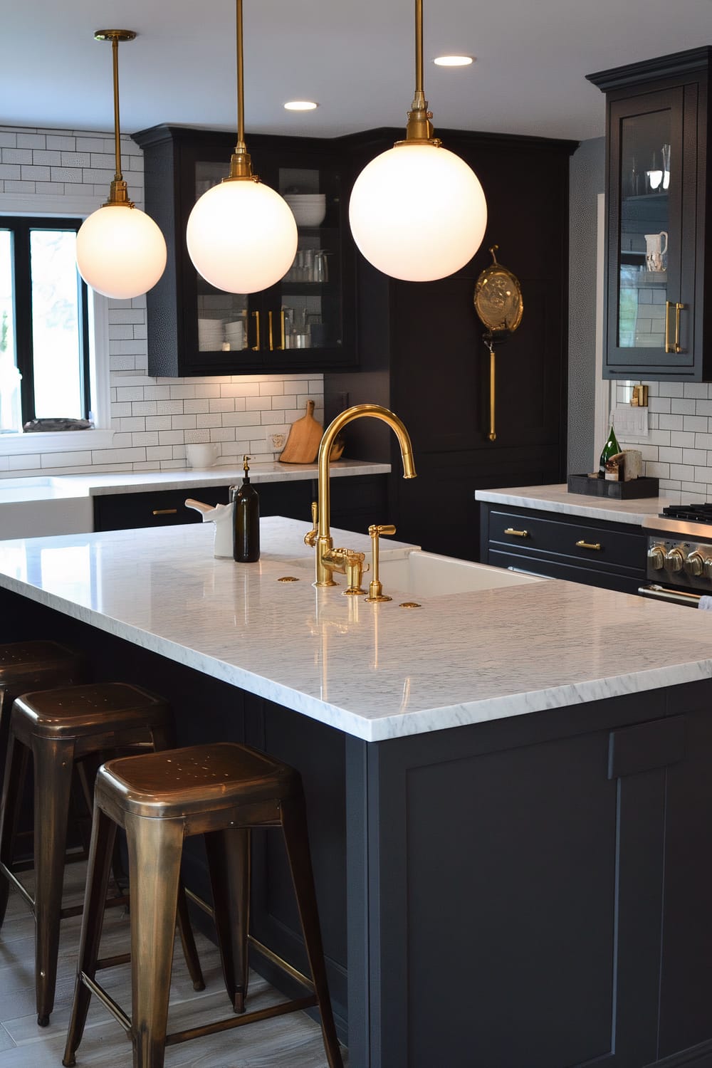 A contemporary kitchen featuring a large white marble countertop with a bronze faucet and matching fixtures, an island with metal bar stools, and dark cabinetry. The walls are adorned with white subway tiles arranged in a brick pattern. Large globe pendant lights hang from the ceiling, adding a soft, warm glow to the space. Some wooden kitchen utensils and olive oil bottle are placed on the countertop.