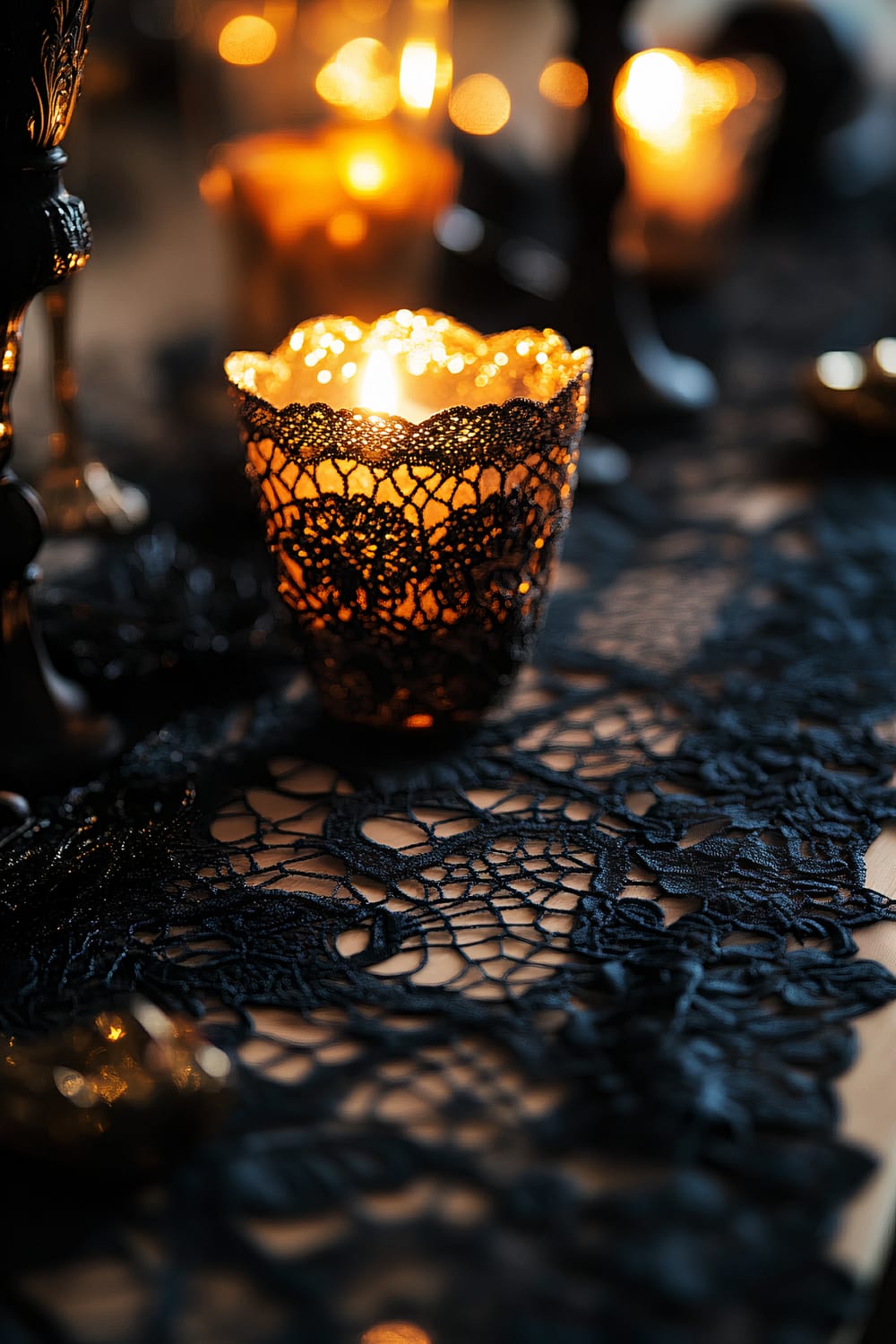 A close-up image of a black lace table runner with intricate patterns and gold metallic accents. A candleholder with a lit candle, also wrapped in black lace, adds a warm glow to the scene, creating an elegant ambiance. The background is uncluttered and softly lit, enhancing the classy Halloween decor.