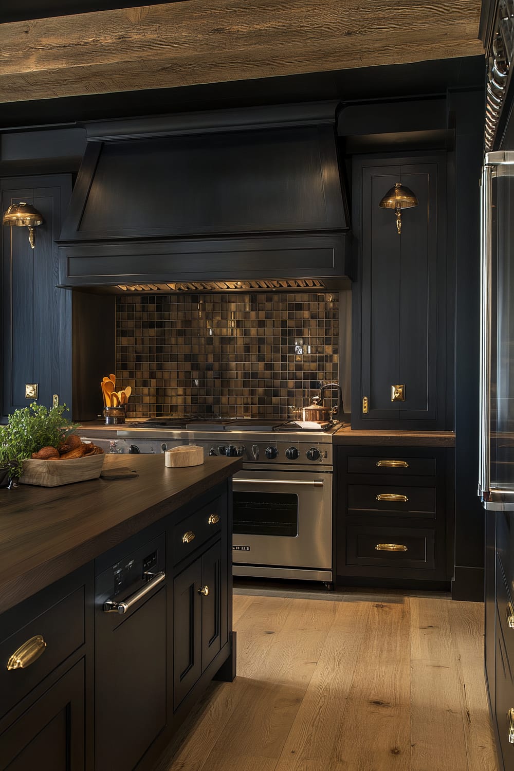 A moody farmhouse kitchen featuring deep charcoal cabinetry, dark walnut countertops, a stainless steel range, and a built-in refrigerator with sleek handles. The kitchen is adorned with vintage-style sconces, a stone backsplash, exposed wooden beams, and has soft, subdued ambient lighting that casts gentle shadows.