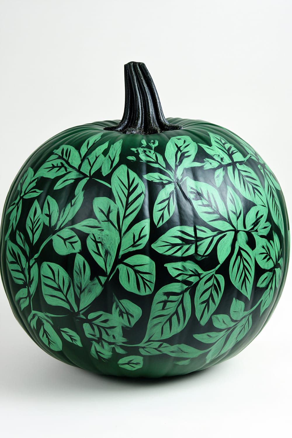 A pumpkin painted in a deep green hue with a black stem. The pumpkin is decorated with intricate green leaf patterns.