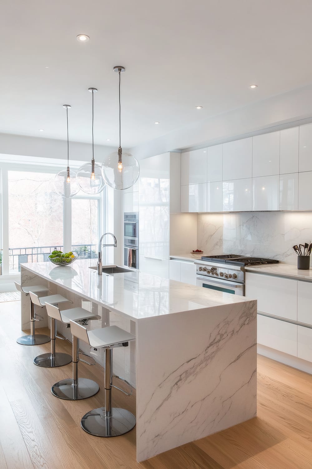 A modern kitchen featuring a central island with a white marble countertop and white cabinetry. There are four contemporary barstools with metallic bases and white seats lined up along one side of the island. Above the island, three glass pendant lights hang from the ceiling. The kitchen also has white high-gloss cabinets and a white marble backsplash. The floor is made of light-colored hardwood, and large windows flood the space with natural light.