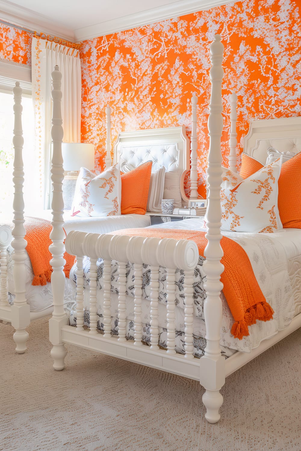 This image showcases a bright and vibrant bedroom with an orange and white color scheme. The room features two twin beds with intricately carved white bedframes and tufted headboards. The beds are adorned with crisp white linens, orange throw blankets, and decorative pillows with white and orange floral patterns. The walls are covered in a bold orange wallpaper with white floral designs, and a full-length window with white drapes allows natural light to fill the room. The design elements create a fresh, lively, and visually stimulating atmosphere.