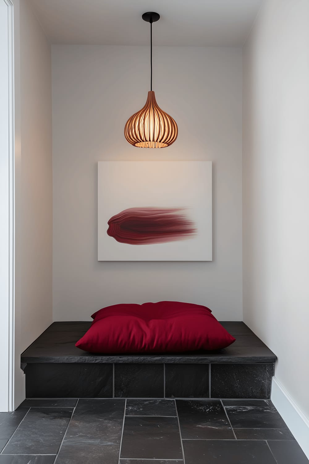 Eye-level view of a peaceful meditation corner displaying a deep red cushion placed on a unique black stone floor. A warm pendant lamp casts a soft glow on the area, while an abstract art piece mounted on a plain white wall serves as the backdrop.