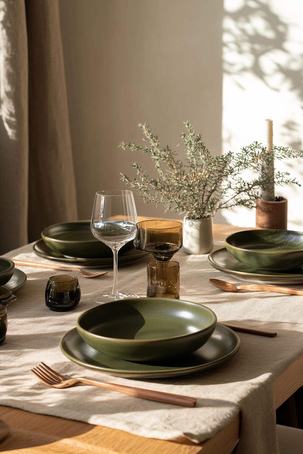 A dining table set in Japandi style, featuring deep green ceramic plates and bowls, wooden cutlery, amber-toned glassware, and natural linen napkins. A small plant in a minimalist vase serves as the centerpiece, and soft natural light creates gentle shadows on the table.