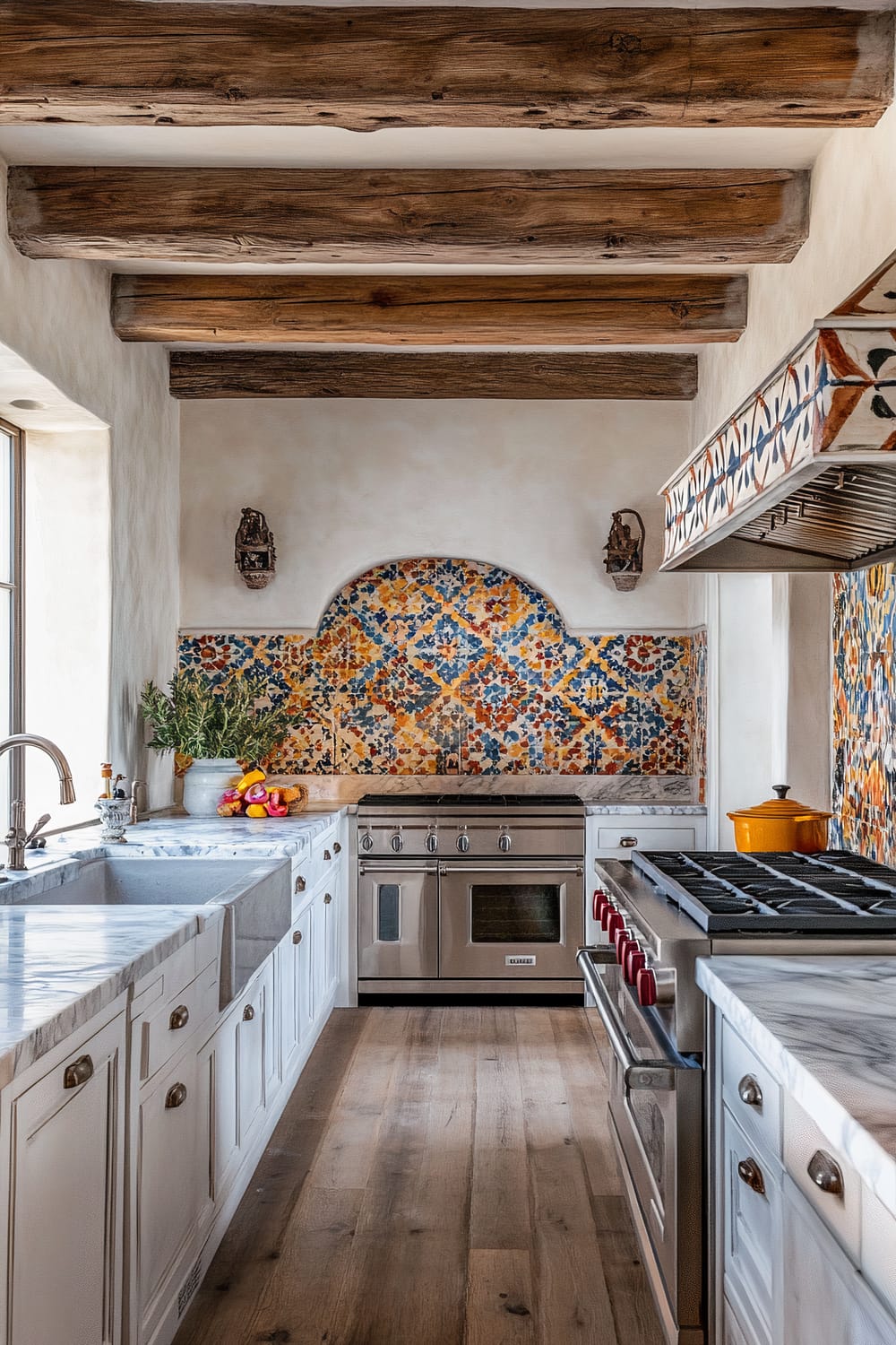 A rustic kitchen features a distinct blend of Southwestern and Mediterranean influences. Exposed wooden beams stretch across the ceiling, setting a warm and earthy tone. Brightly colored tile backsplash, with patterns of blue, yellow, and orange, forms an arched design behind a stainless steel oven range. White cabinets with marble countertops line both sides of the narrow kitchen. A farmhouse sink and a potted plant adorn the left counter, while the right counter hosts a modern stovetop. A wooden floor furthers the rustic charm, complementing the natural elements beautifully.