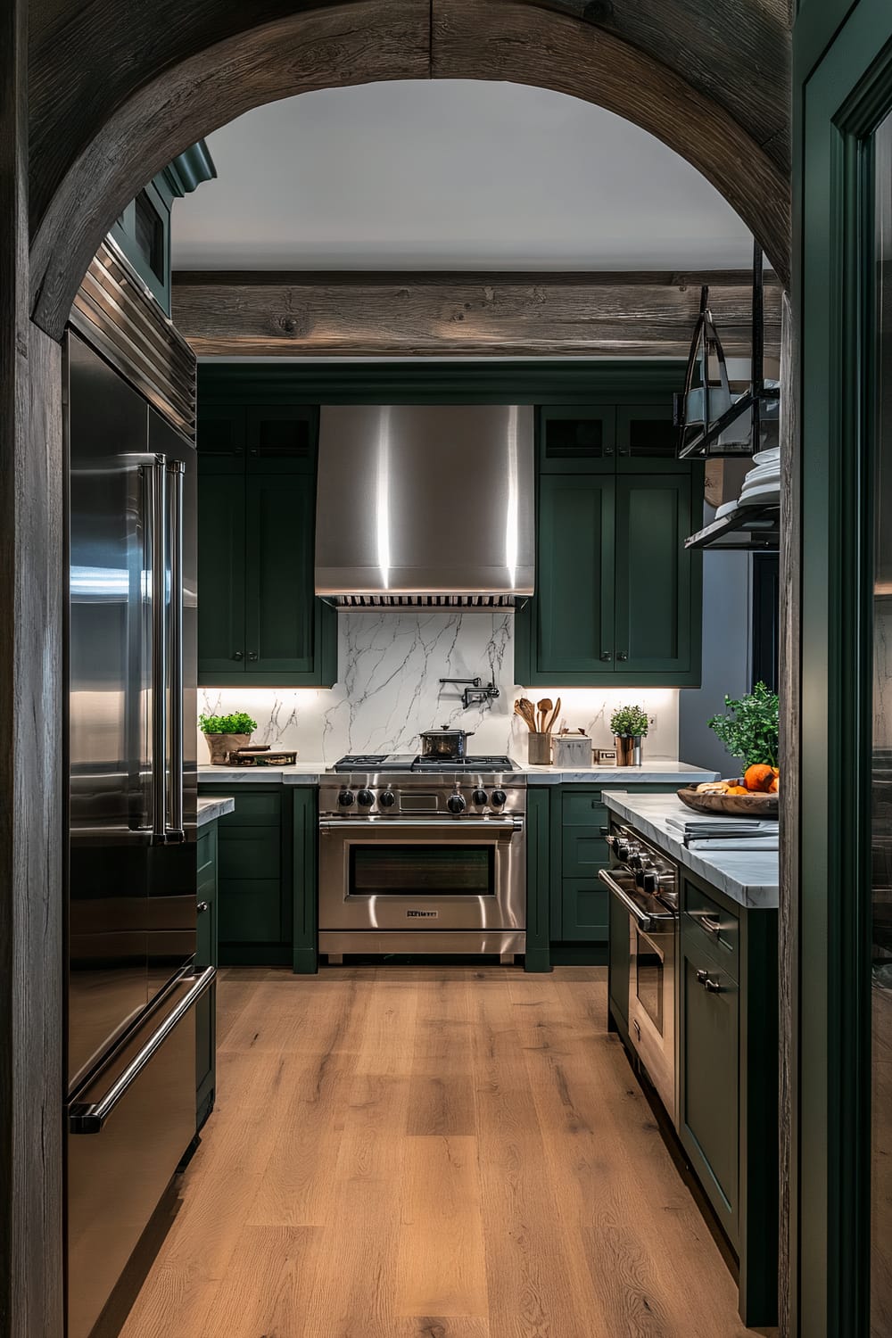 An atmospheric farmhouse kitchen viewed through an open arch doorway, featuring dark green cabinets, white marble countertops, stainless steel appliances, and layered lighting with overhead fixtures and under-cabinet lights.