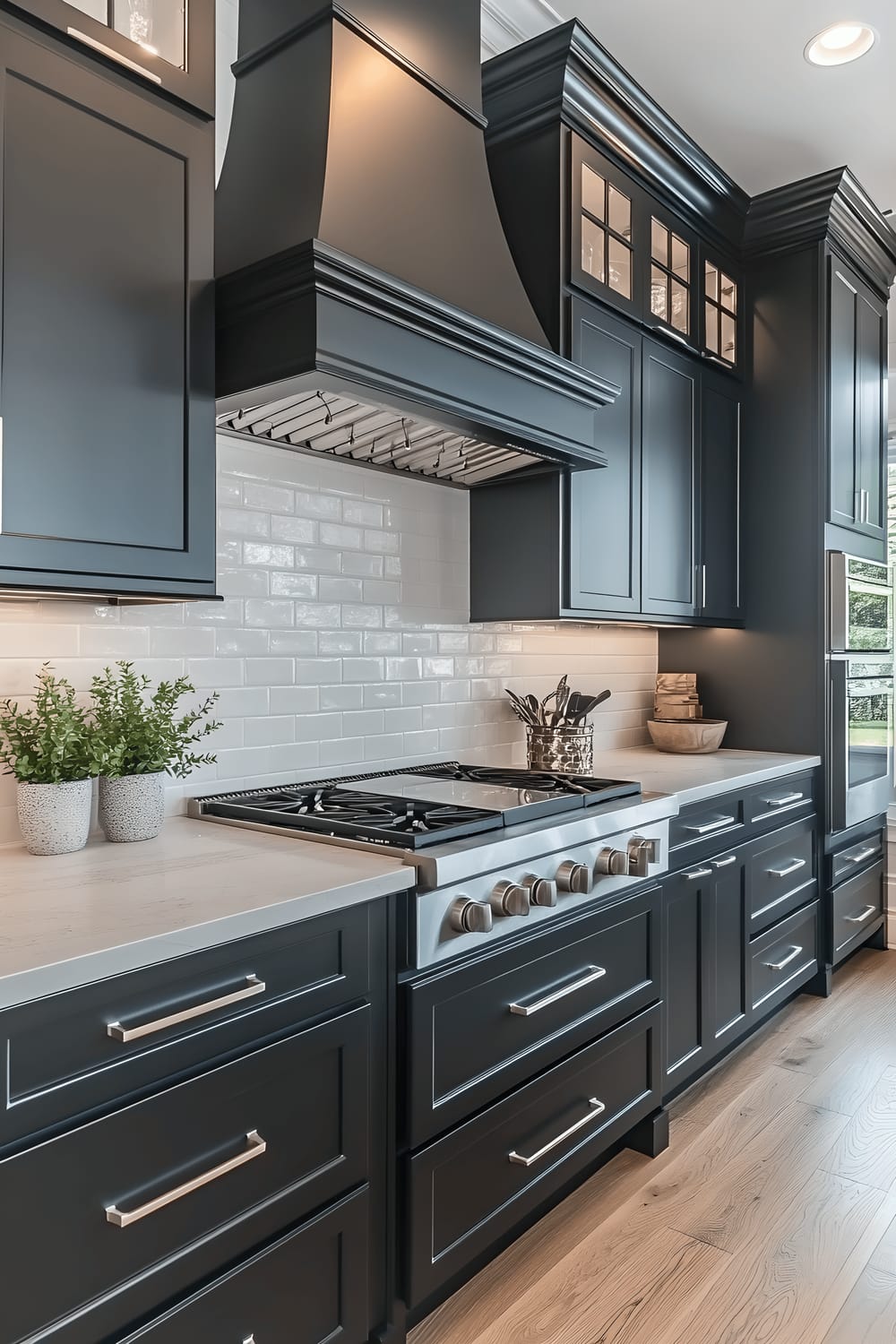 A low-angle view of a kitchen featuring matte black cabinetry, sleek white marble countertops, stainless steel fixtures, under-cabinet LED lighting, and a single potted eucalyptus plant adding a touch of nature.