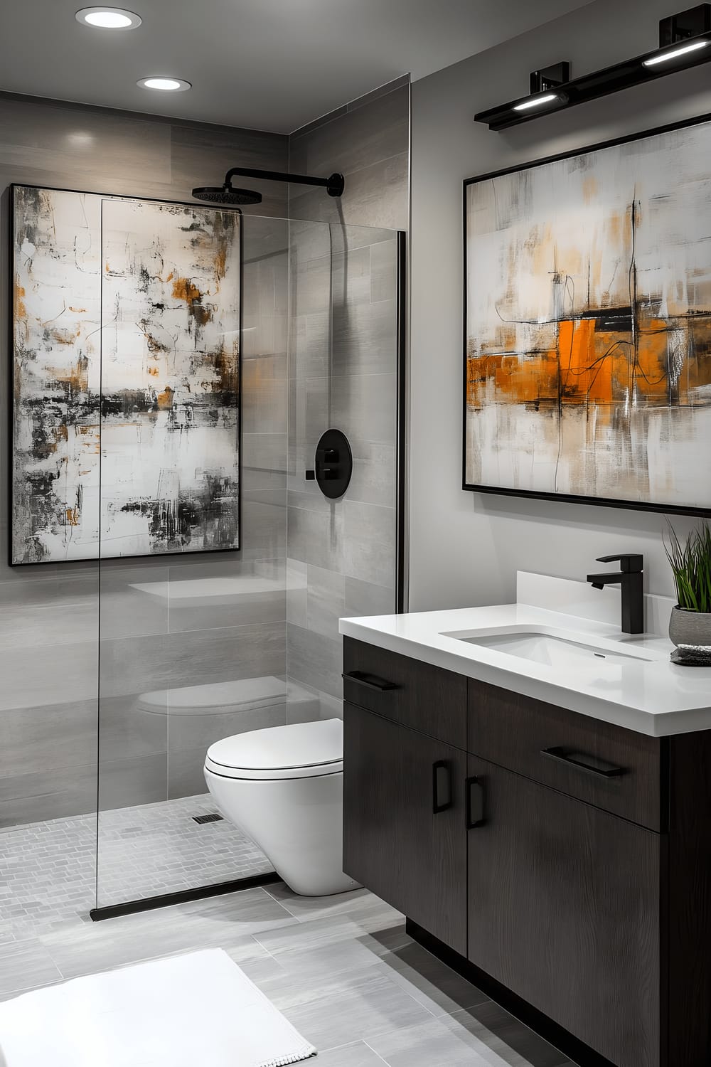 An urban contemporary bathroom featuring sleek gray tiles on the floor and the walls. A modern floating vanity in dark walnut is centrally positioned, beneath a large mirror with an abstract art piece above. A frameless glass shower enclosure is to the right. Fixtures throughout the bathroom are minimalist and black in color, complementing the darker tones of the vanity and contrast against the gray surrounding. Downward facing, brightly lit wall lamps highlight the design elements.