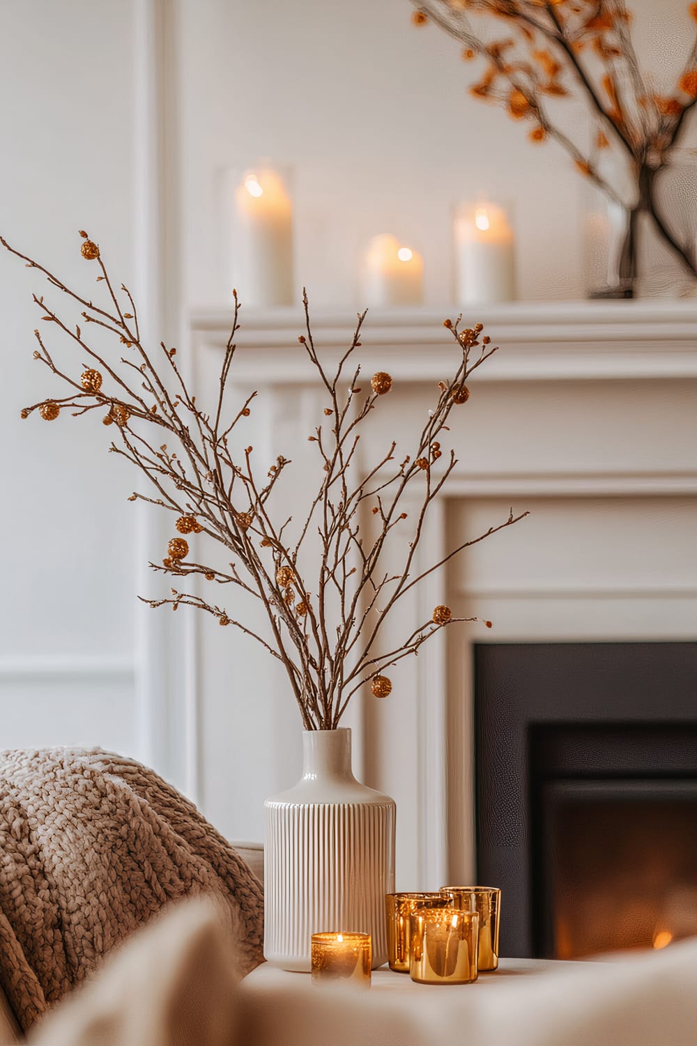 A white ceramic vase with vertical ridges holds winter branches adorned with golden berries, set on a table beside golden votive candles. In the background, a mantle with lit ivory candles and additional branches of orange berries is visible, casting a warm, inviting ambiance.