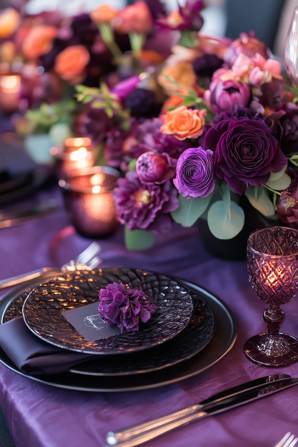 A monochromatic Thanksgiving table setting featuring shades of deep purple, with textured linens, matte and glossy ceramic tableware, a floral centerpiece with contrasting purple and orange flowers, and candlelight providing sophisticated moody lighting.