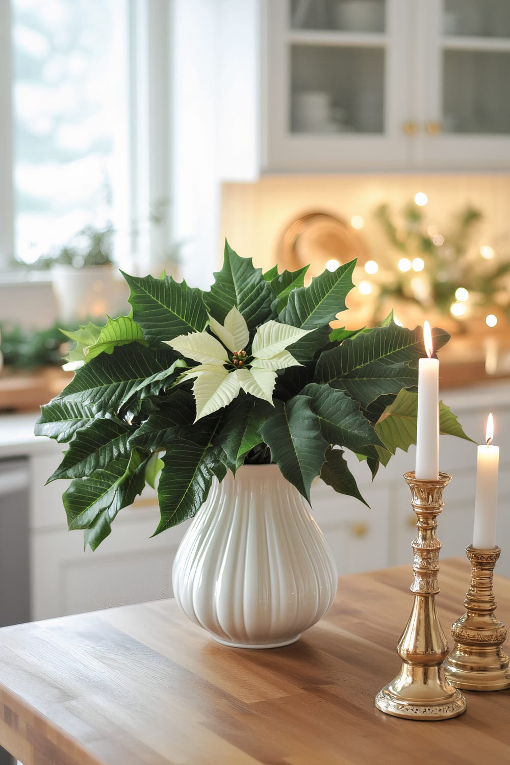 A modern farmhouse kitchen with a green and white theme, featuring a lush green poinsettia in a white ceramic vase on a wooden countertop. The setting includes white candles on gold candle holders and soft natural lighting.