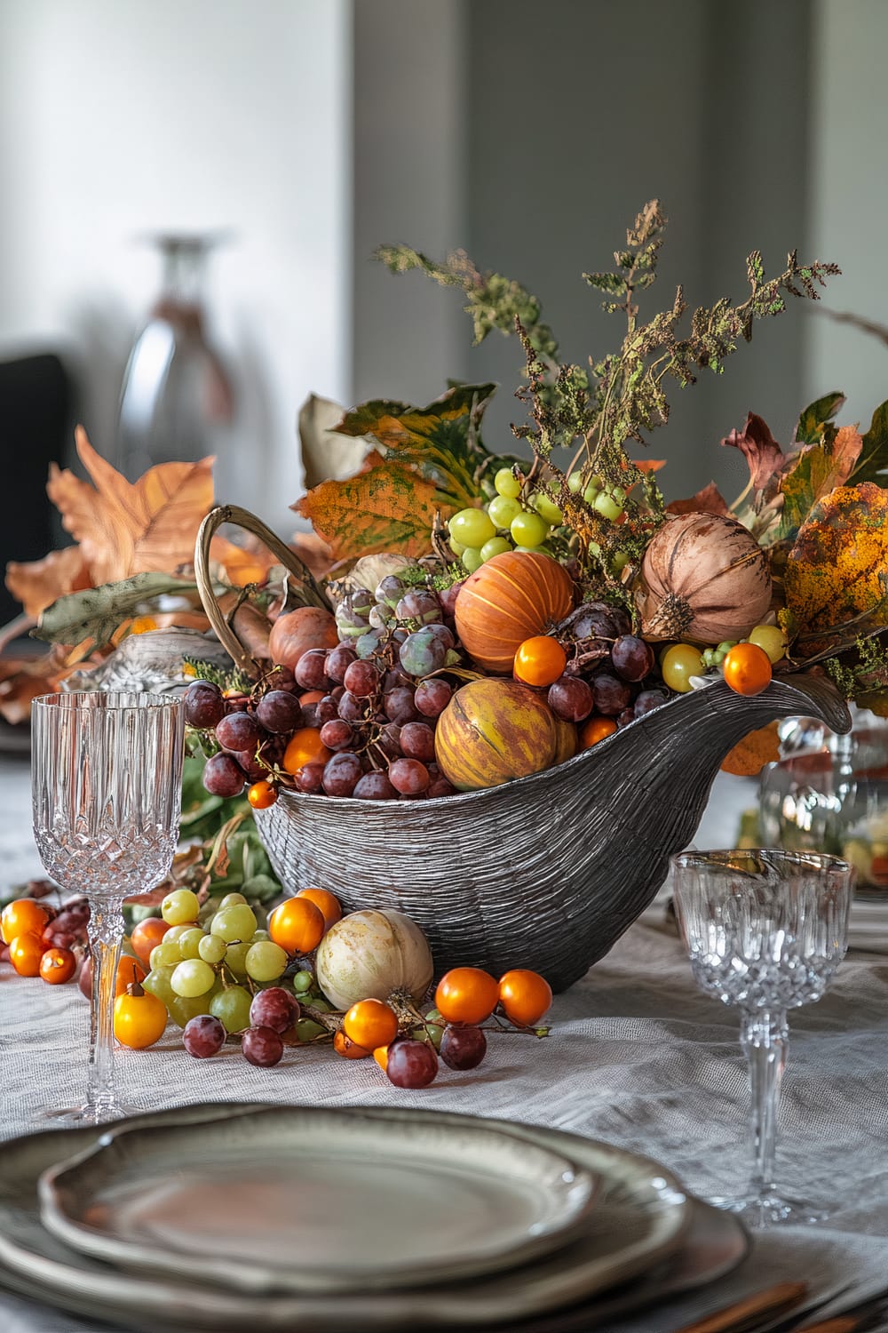 An elegant table setting with a centerpiece featuring a cornucopia filled with assorted autumn fruits, such as grapes, miniature pumpkins, and decorative foliage. The table is adorned with crystal glasses and neutral-toned plates, with a soft, textured tablecloth underneath.