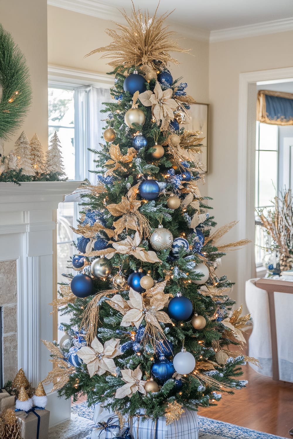 A beautifully decorated Christmas tree adorned with blue, gold, and white ornaments, including spherical baubles, glittery poinsettia flowers, and gold foliage. The top of the tree features a striking gold starburst tree topper. Surrounding the tree are wrapped presents and festive decorations, creating a warm and inviting holiday ambiance.