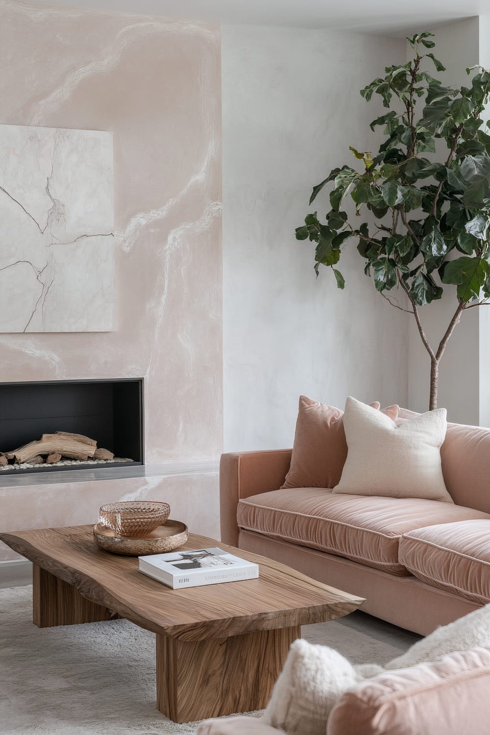 A living room with a blush-pink velvet sofa, a sculptural wooden coffee table, a fireplace with a marble surround, and a large plant in the corner.