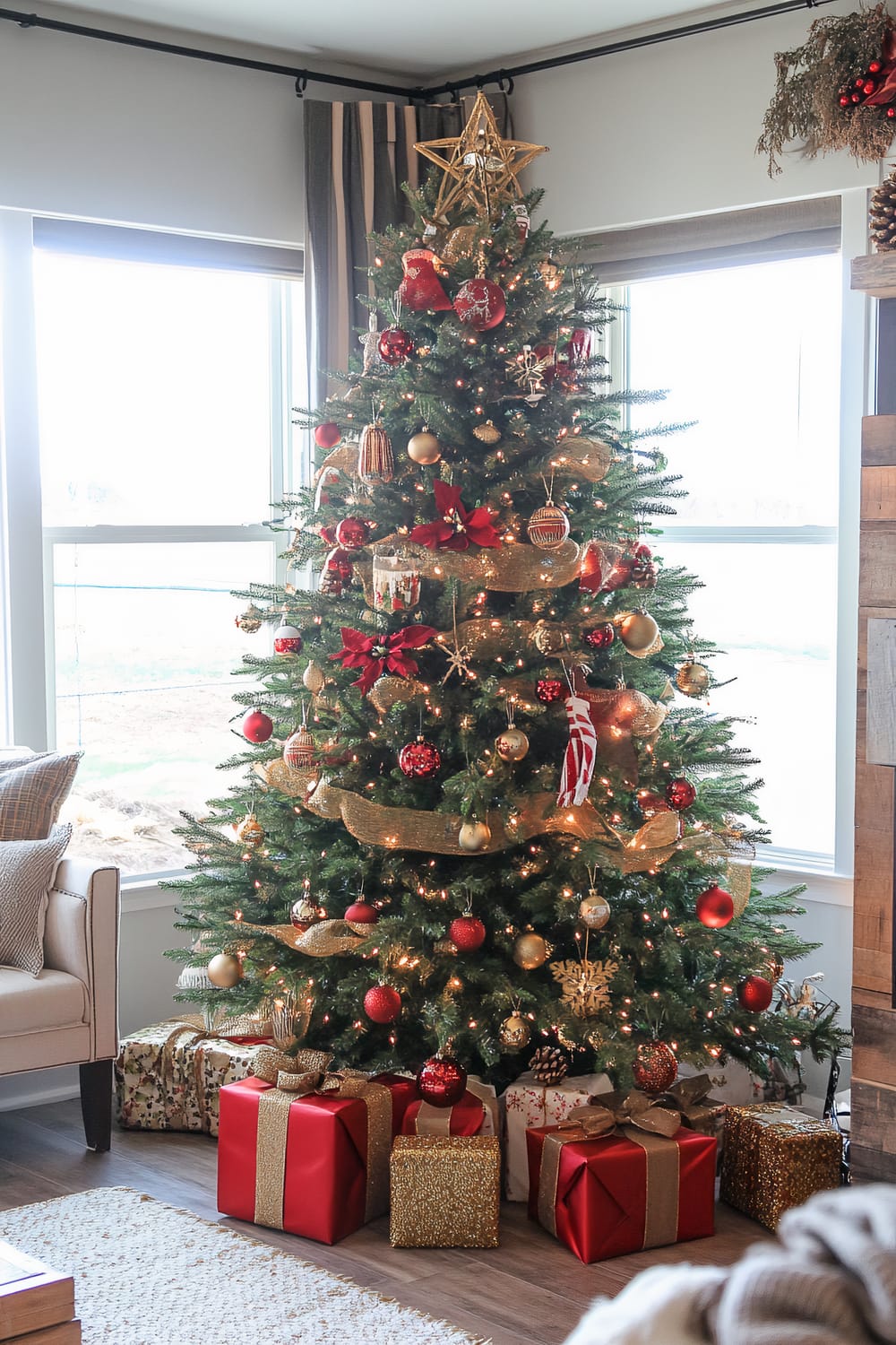 A decorated Christmas tree stands in a well-lit room. The tree is adorned with various ornaments in gold and red, including baubles, ribbons, and a star at the top. There are wrapped gifts with shiny bows under the tree. Furniture and other holiday decor are visible in the background.