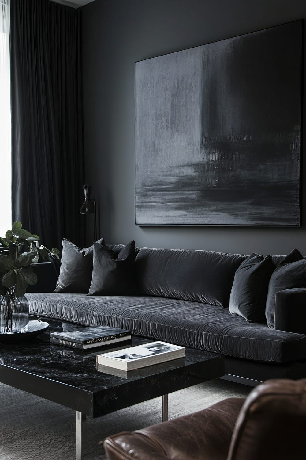 A moody living room with dark gray walls, a deep charcoal sofa, a black-and-white abstract painting above the sofa, a black marble coffee table with minimalist decor, a distressed brown leather armchair, large potted plant, and natural light from wide windows.