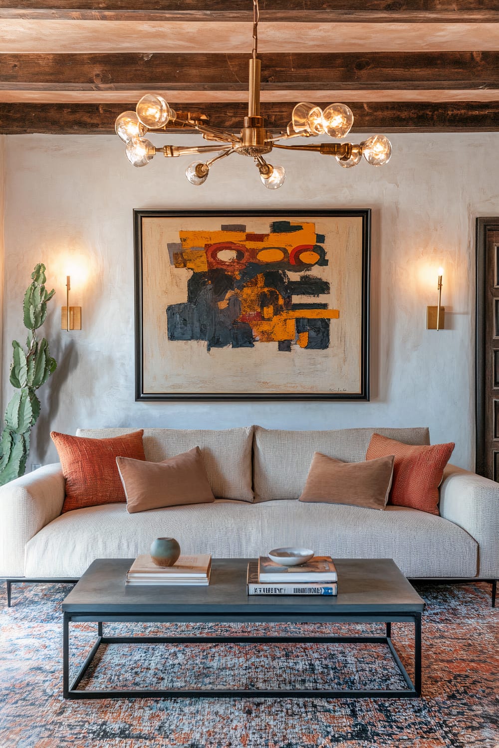 Living room with vintage and retro elements. Features a neutral-colored sofa with pillows, a vintage coffee table with books and a small decorative item, and a colorful abstract painting on the wall above the sofa. The room is illuminated by a classic chandelier and two wall-mounted lights. A cactus plant is placed beside the sofa.