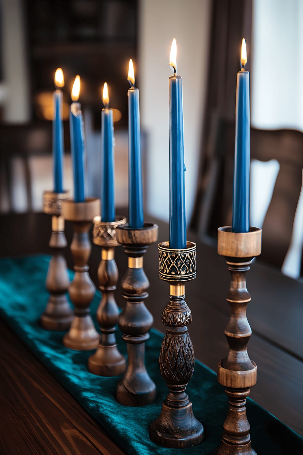 A striking dining room scene featuring a centerpiece of repurposed wood candlesticks of varying heights with intricate brass detailing, each holding a cobalt blue taper candle. The candles offer a warm golden glow to the surrounding area. The centerpiece is placed on a dark wooden table adorned with a lush deep green velvet runner. The table stands against the background of a softly lit, elegant dining room, the ambient lighting illuminating the textures of the wood and the shine of the brass.