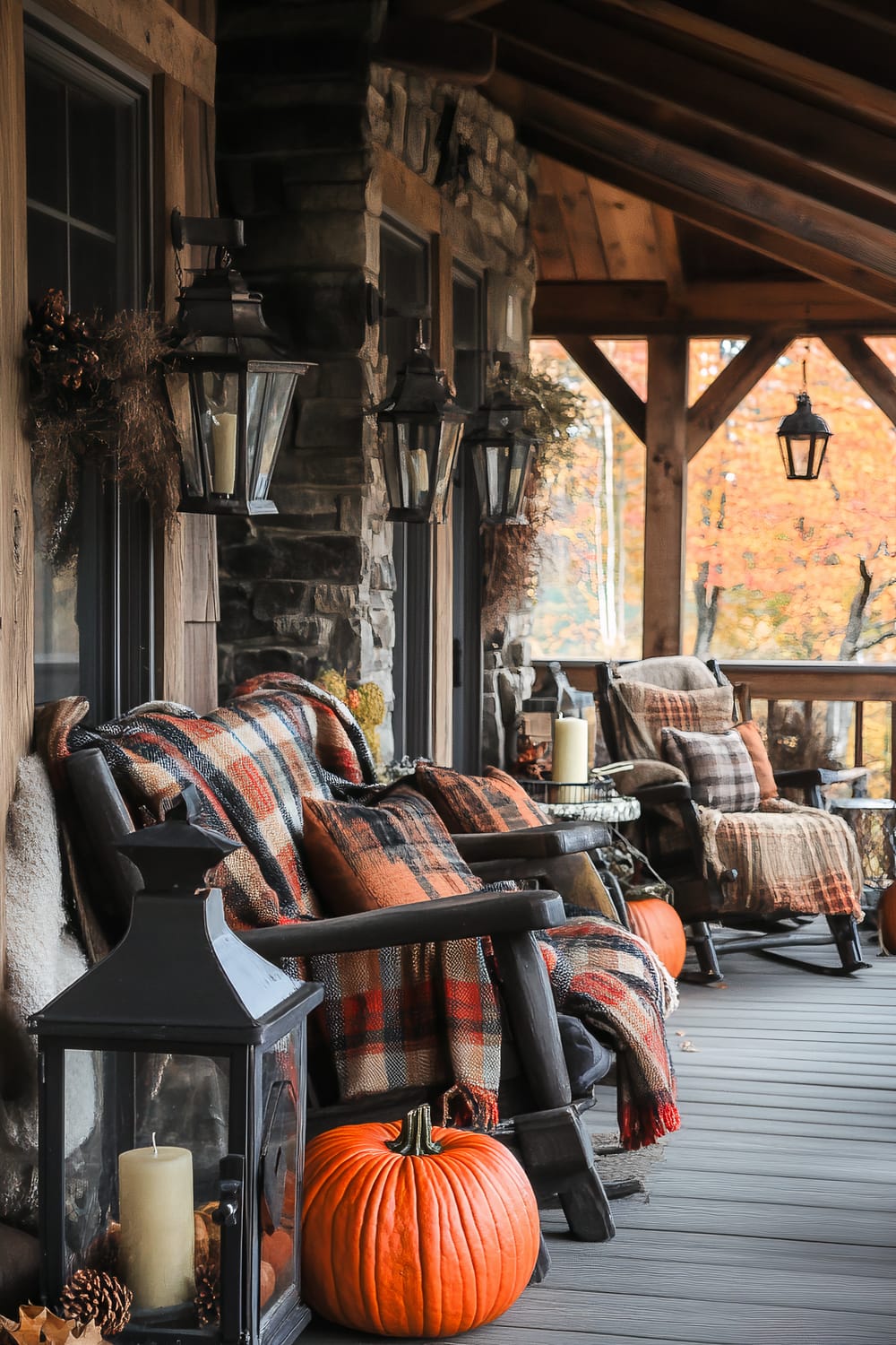 A rustic porch adorned for autumn. The porch features wooden rocking chairs draped with orange and plaid checkered blankets and cushions. Large black lanterns with candles inside are placed beside bright orange pumpkins. The stone facade, wooden beams, and framed windows enhance the porch's warm and inviting aesthetic. Fall foliage in the background adds a touch of seasonal color.