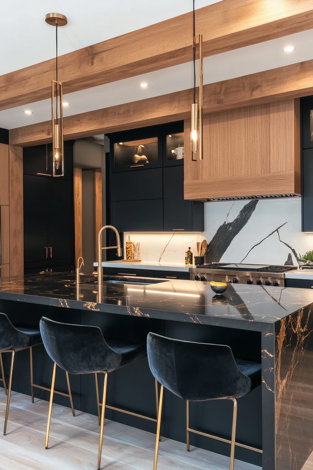 A sophisticated kitchen characterized by black and wood elements. The central island boasts a black marble countertop with gold veining, complemented by a sleek black sink and gold faucet. Above the island hang two modern pendant lights in a gold finish. Towards the left, the kitchen cabinetry features a blend of black and wooden textures, while a dramatic marble backsplash with black streaks provides a striking focal point. The bar area includes black velvet chairs with golden legs, set against a backdrop of matching cabinetry. The ceiling displays wooden beams that enhance the room's warm and elegant aesthetic.