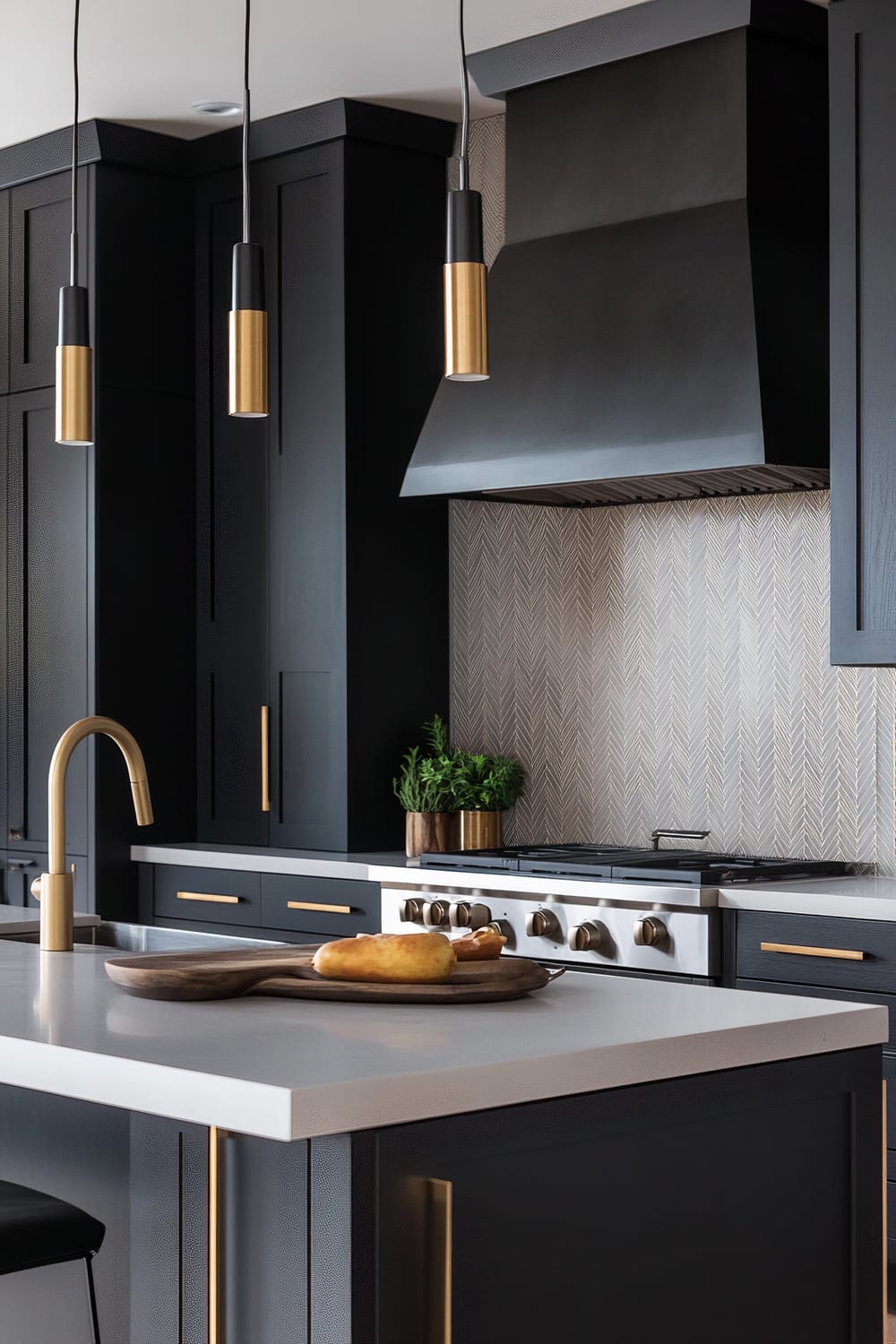 The image shows a modern kitchen with dark cabinetry and gold accents. A central island has a white countertop with a wooden cutting board holding bread. Three pendant lights with black and gold design hang above the island. A matte black range hood is set against a herringbone-patterned backsplash, and the oven and stove are integrated seamlessly into the cabinetry.