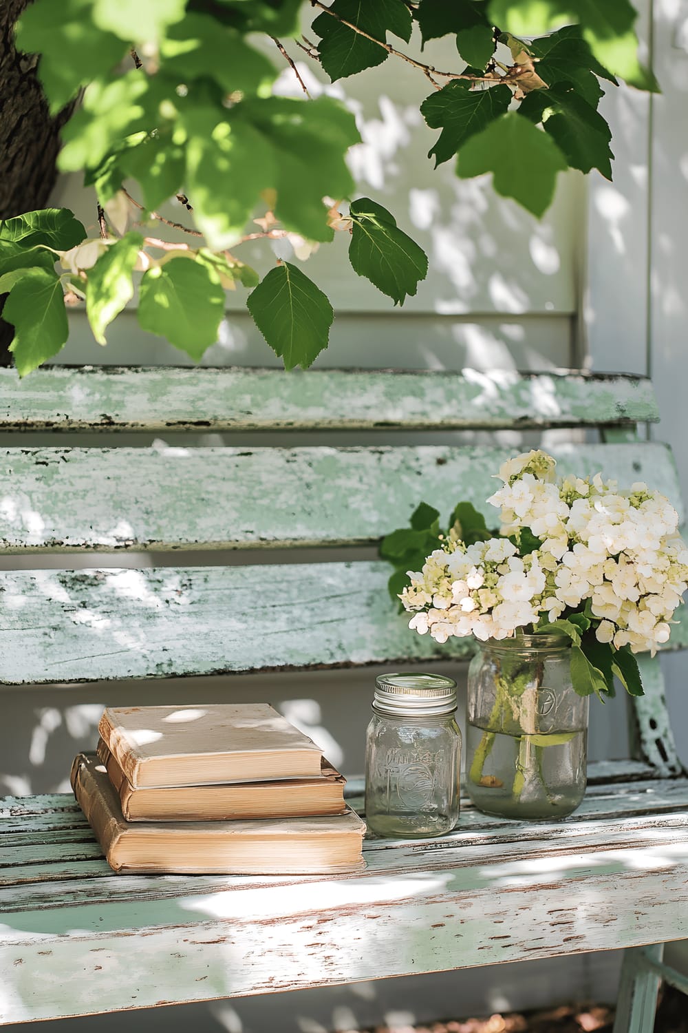 A romantic outdoor scene depicts a worn antique bench, alongside which rests a neat stack of age-old books and a simple, yet charming, floral arrangement in a mason jar. The dappled sunlight filtering through overhanging branches imparts an enchanting aura, highlighting the beauty of the variegated paint on the bench and lending an almost ethereal glow to the tableau.