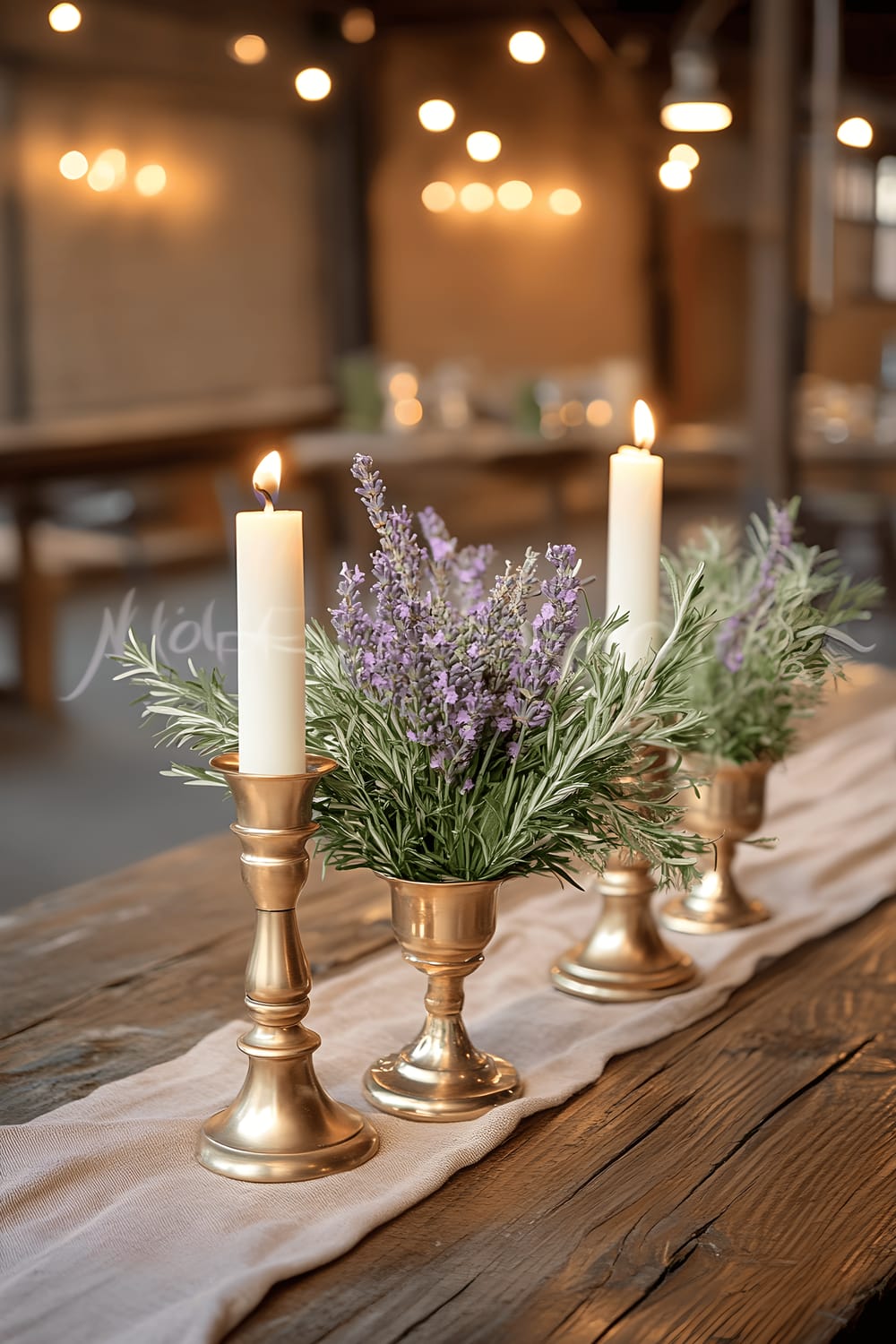 A rustic wooden table featuring a luxurious centerpiece of three champagne gold candle holders filled with fresh sage, rosemary, and lavender sprigs. A soft apricot table runner underlines the arrangement. The ambiance is highlighted by subtle overhead lighting.