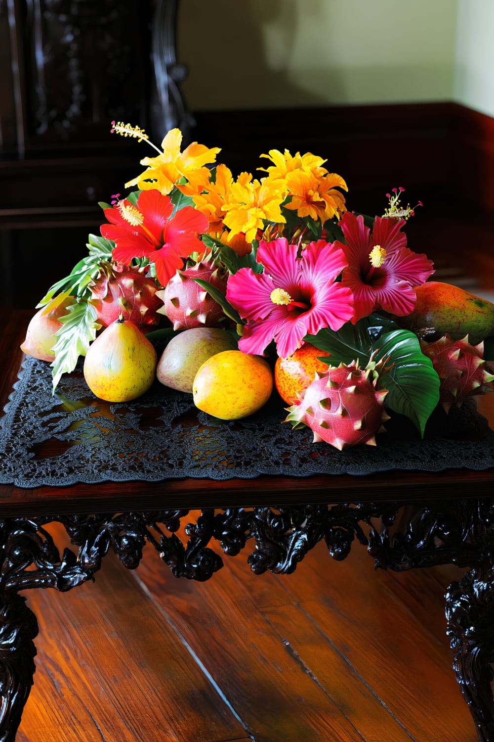 Image of an ornate wooden table with a black lace doily, adorned with an arrangement of vibrant tropical flowers and fruits, including yellow, pink, and red hibiscus flowers, along with mangos, and possibly dragon fruits and papayas.