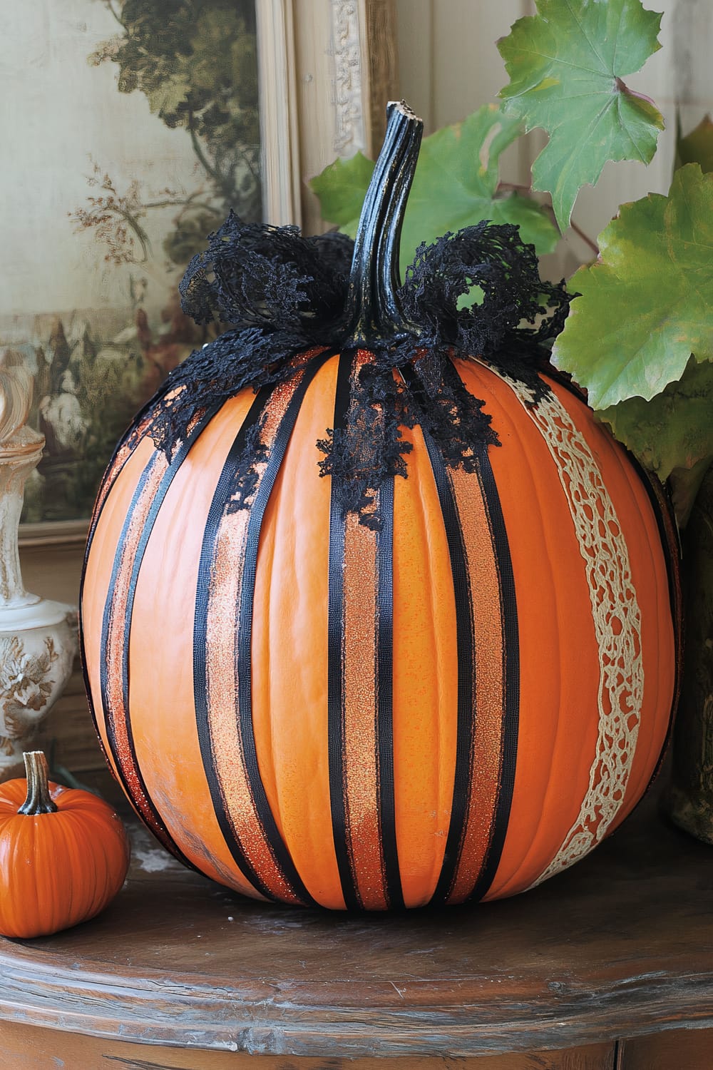 An elaborately decorated pumpkin is showcased on a wooden surface. The large pumpkin features black lace and orange glitter stripes, and a portion covered with a vertical band of white lace. It has a distinct, curvy stem adorned with black lace. Surrounding it are leafy green plants and a smaller, undecorated pumpkin.