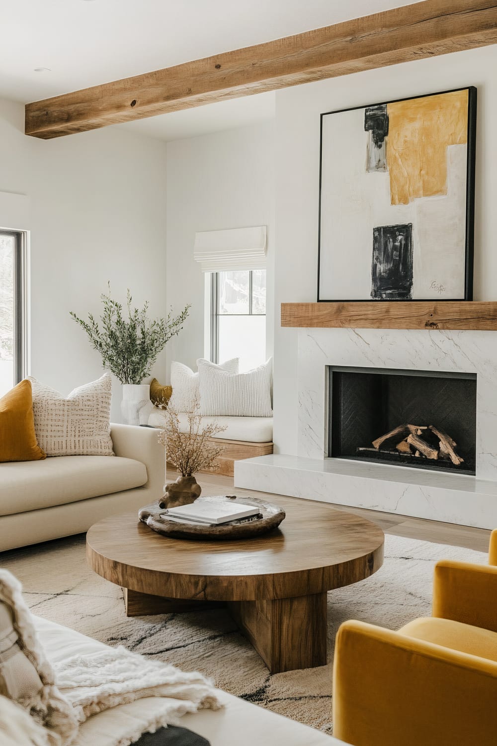 An inviting modern living room with a plush cream sofa, a round wooden coffee table, a yellow armchair, built-in benches with pillows, a marble-framed fireplace, abstract art above the mantel, and sculptural decor elements.