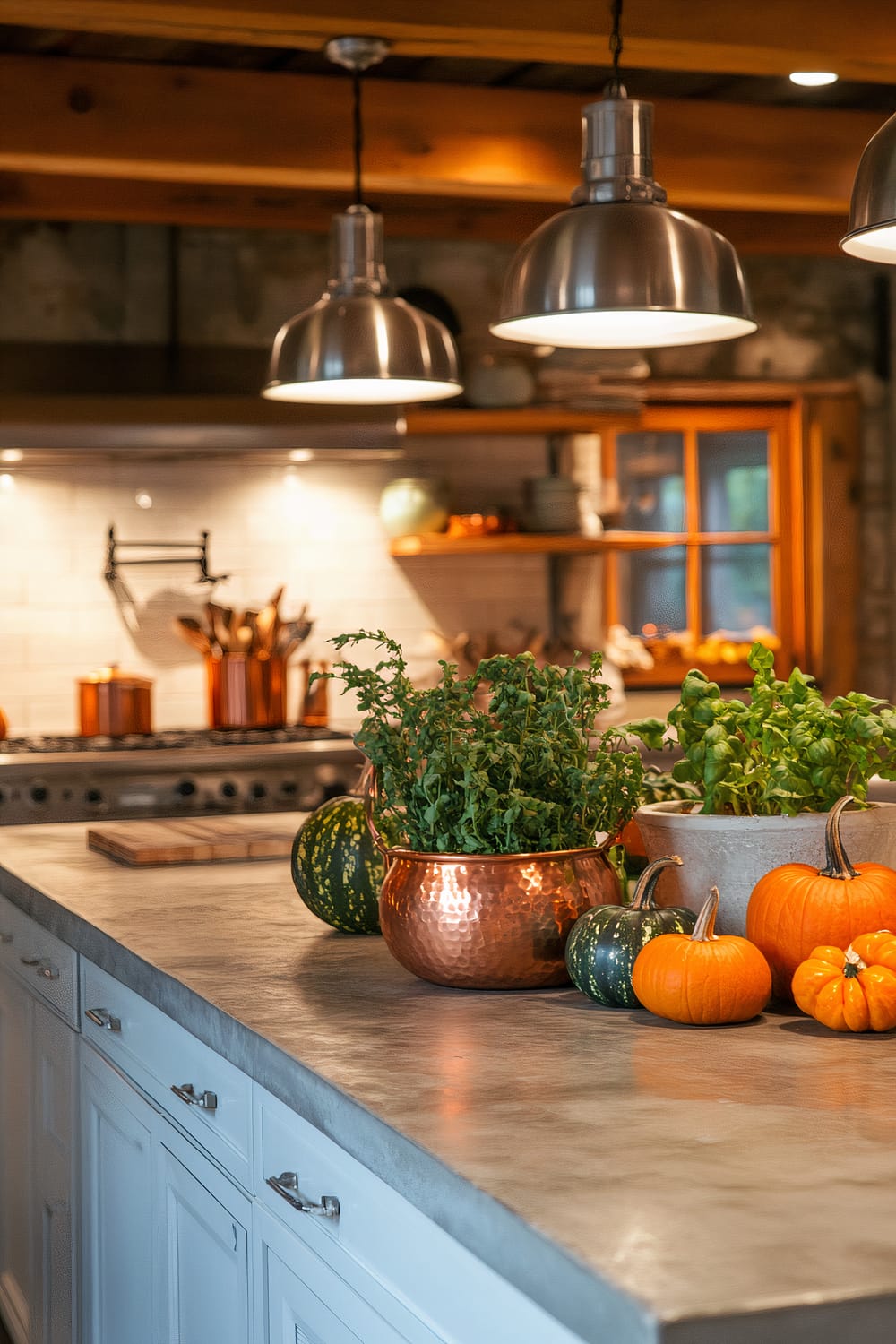 An industrial-modern kitchen with exposed steel beams, a sleek concrete countertop, and minimalist white cabinetry. Large copper pots with autumn herbs and small ceramic pumpkins in green and orange are placed on the countertop. Stainless steel appliances and white tiles add to the clean look. Pendant lights provide warm illumination to the space.