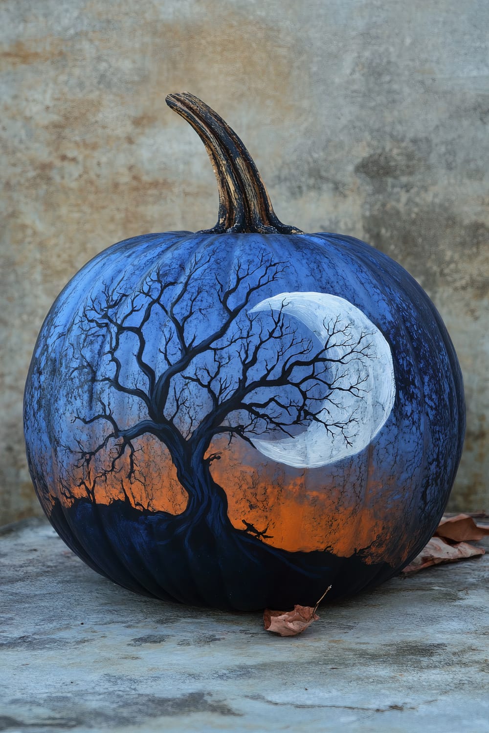 A pumpkin painted with a vivid scene of a full moon rising against an orange and blue sunset sky. Leafless, intricate tree branches stand silhouetted against the moon.