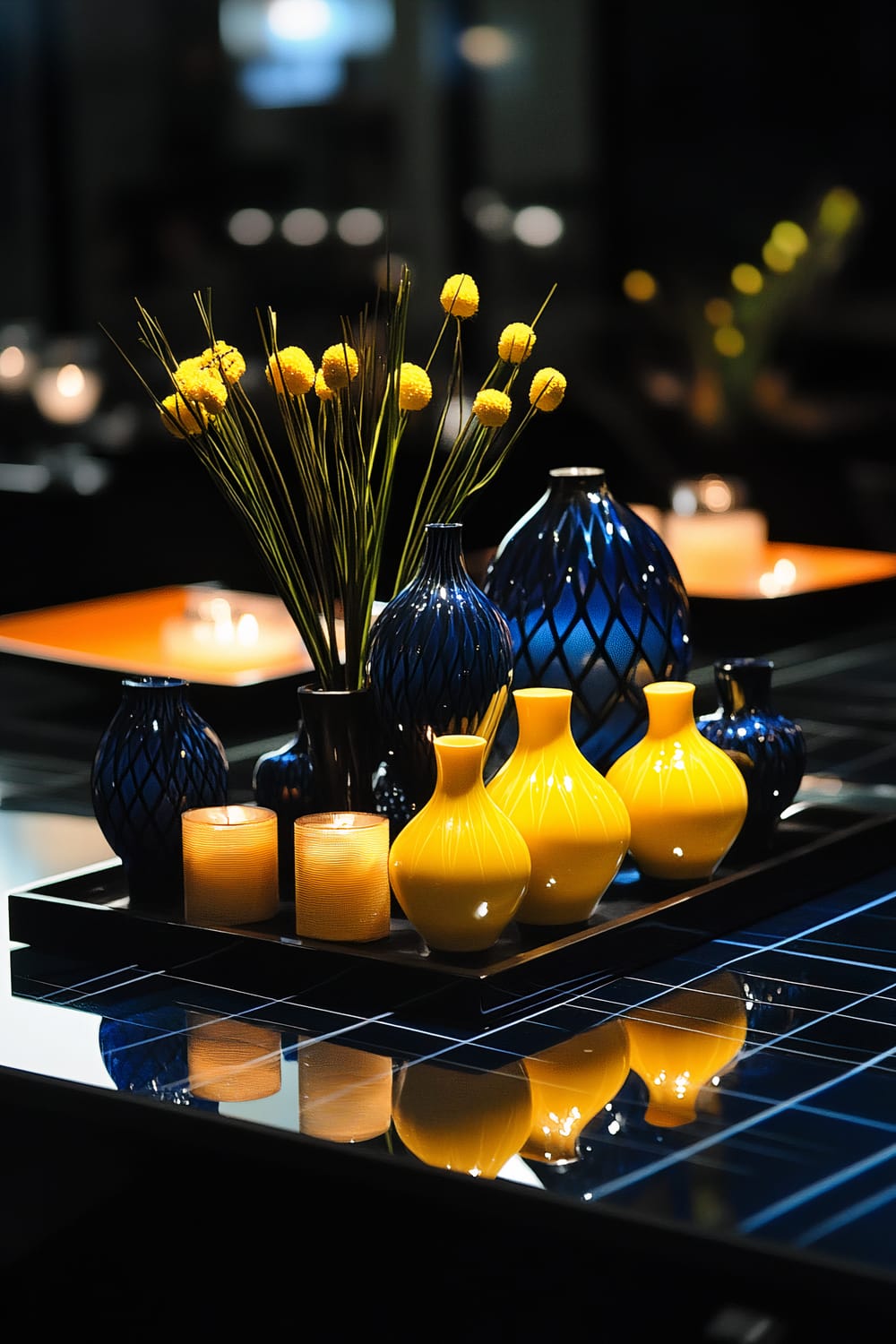 A modern geometric centerpiece featuring mustard yellow and cobalt blue vases and candles arranged on a sleek black tray. The setup is illuminated by strategic lighting, casting dynamic shadows and emphasizing the bold colors and contemporary design.