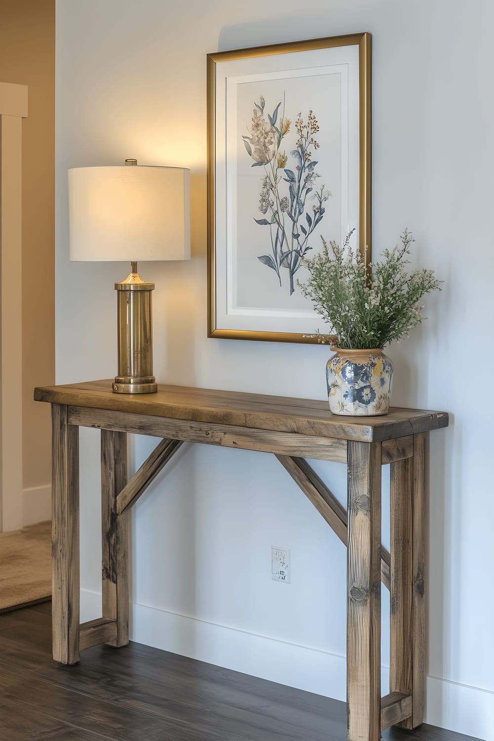 A modern farmhouse-style entry hall bathed in natural light. There is a reclaimed-wood console table with a vintage brass lamp and a framed botanical print on it, and a window nearby that allows daylight to fill the space.