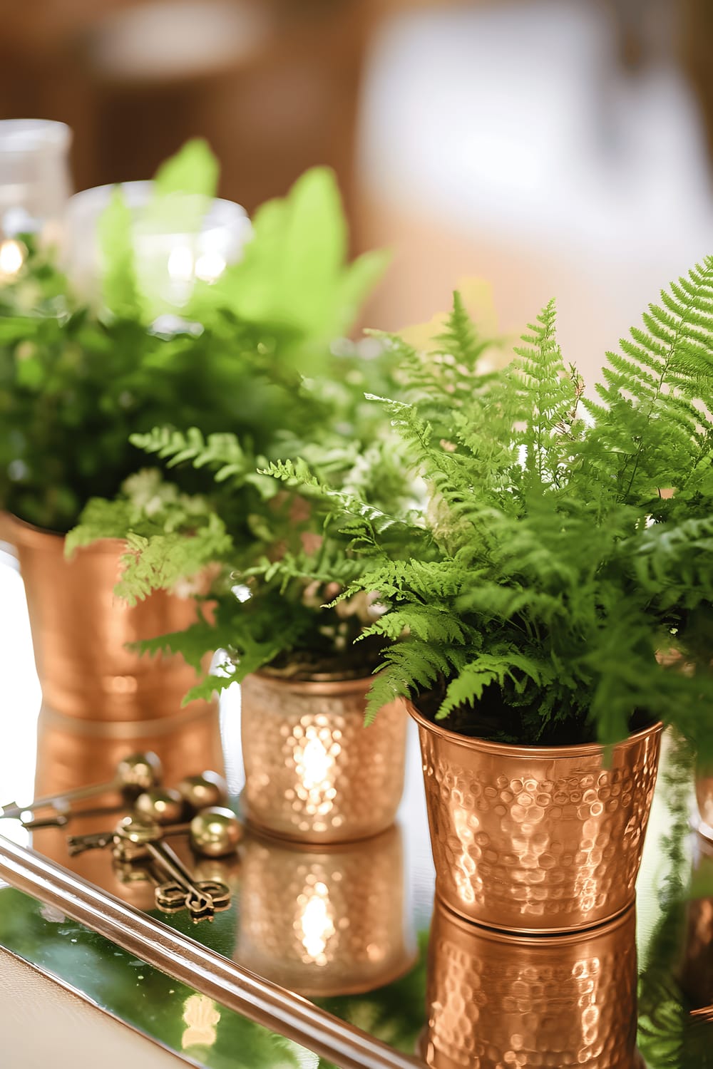 A sophisticated vintage-inspired centerpiece on a kitchen table, composed of a collection of vintage copper pots brimming with lush greenery such as ferns and ivy. Various tiny decorative elements like antique keys, glass beads, and miniature lanterns are interspersed throughout. The entire arrangement is placed on a mirrored tray set atop a soft, neutral-colored table runner, and it is accentuated by warm, directional lighting that showcases the copper tones and vibrant green plants.