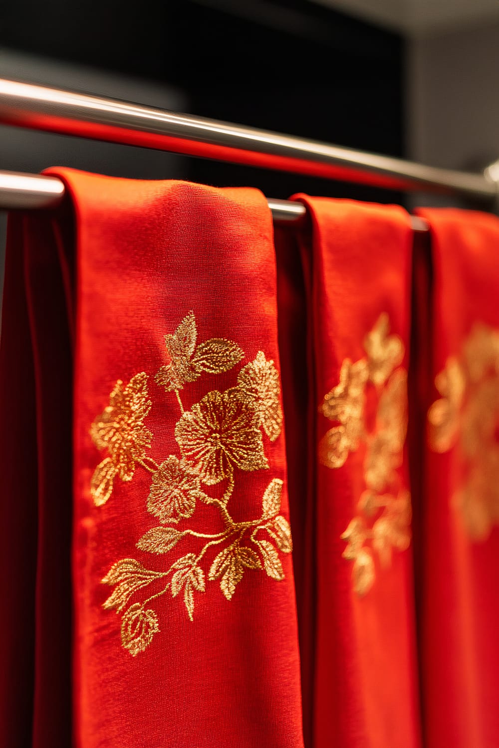 A close-up of bright red dish towels with intricate gold embroidered patterns hanging on a sleek stainless steel rod in a modern kitchen. The towels are vividly illuminated, highlighting the rich red color and shimmering gold designs. The background is minimalistic, ensuring the towels are the focal point.