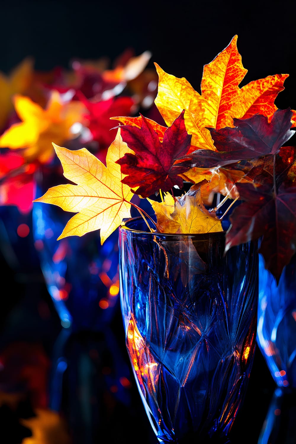 Vibrant cobalt blue glass vases filled with a mix of deep red and golden yellow autumn leaves. The warm light illuminates the leaves, creating a striking contrast and dynamic visual flow.