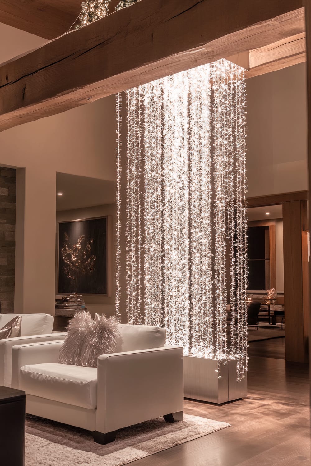 A luxurious living room featuring a white crystal icicle garland hanging from a polished wooden beam, illuminated by soft spotlights. The garland cascades down beside crisp white armchairs adorned with metallic silver pillows. The space is elegantly decorated with warm wooden accents and ambient lighting.