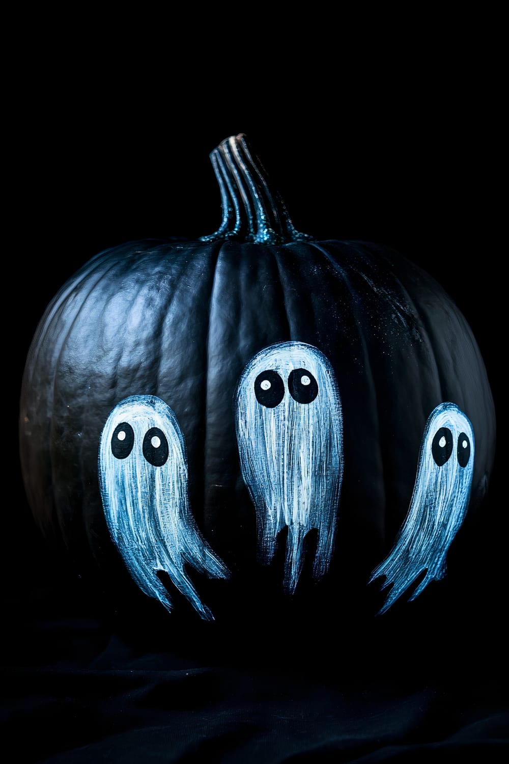 A black pumpkin with a glossy surface is decorated with three painted ghost figures. The ghosts are depicted as white, elongated shapes with large, black, oval eyes, standing out sharply against the dark background. The scene captures a spooky, yet playful Halloween ambiance.