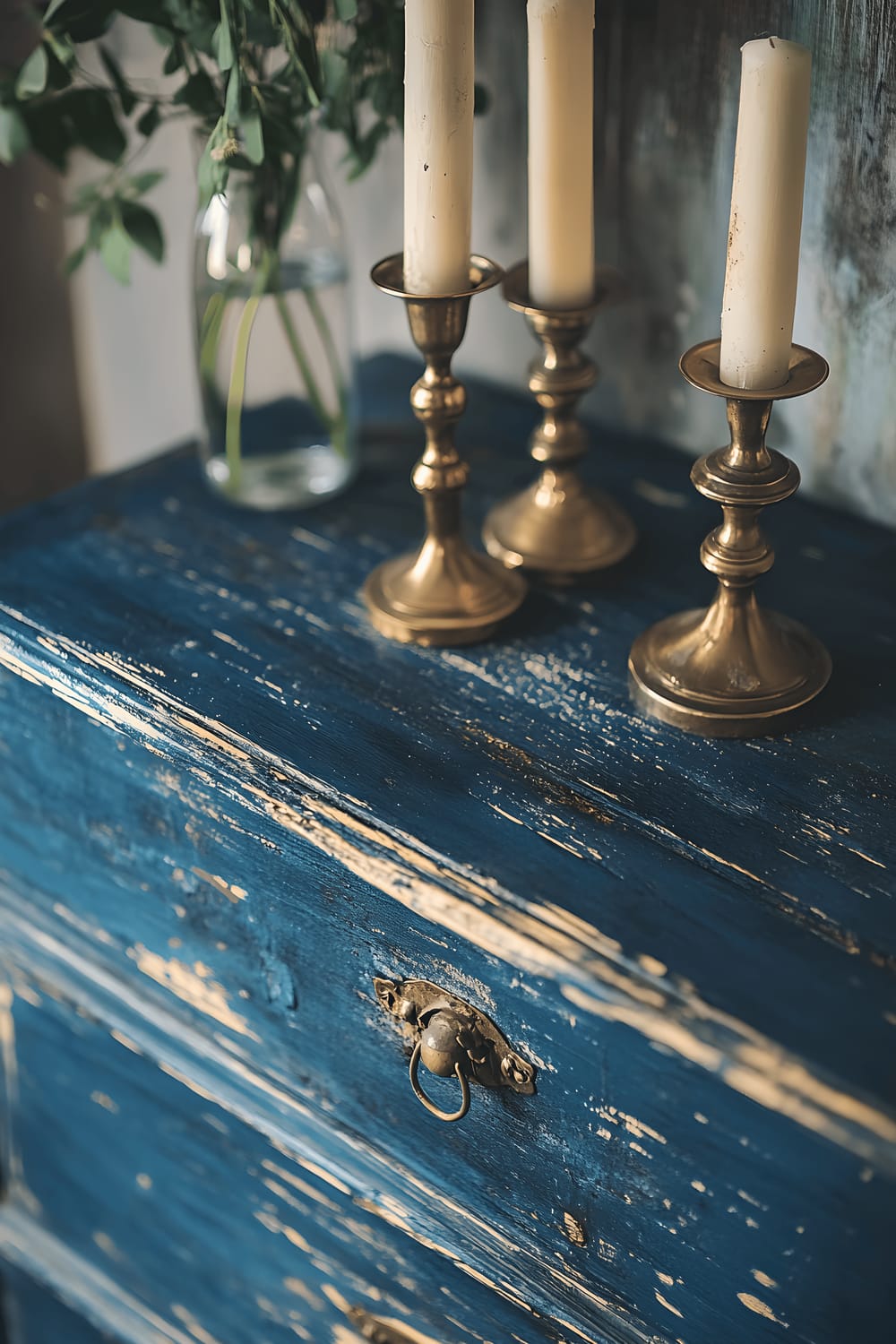 A repurposed wooden dresser, painted in a deep shade of indigo. The dresser's distressed edges reveal past layers of paint, telling a story of its history. The dresser is styled with vintage brass candlesticks that cast a soft, warm light, adding an inviting ambience.