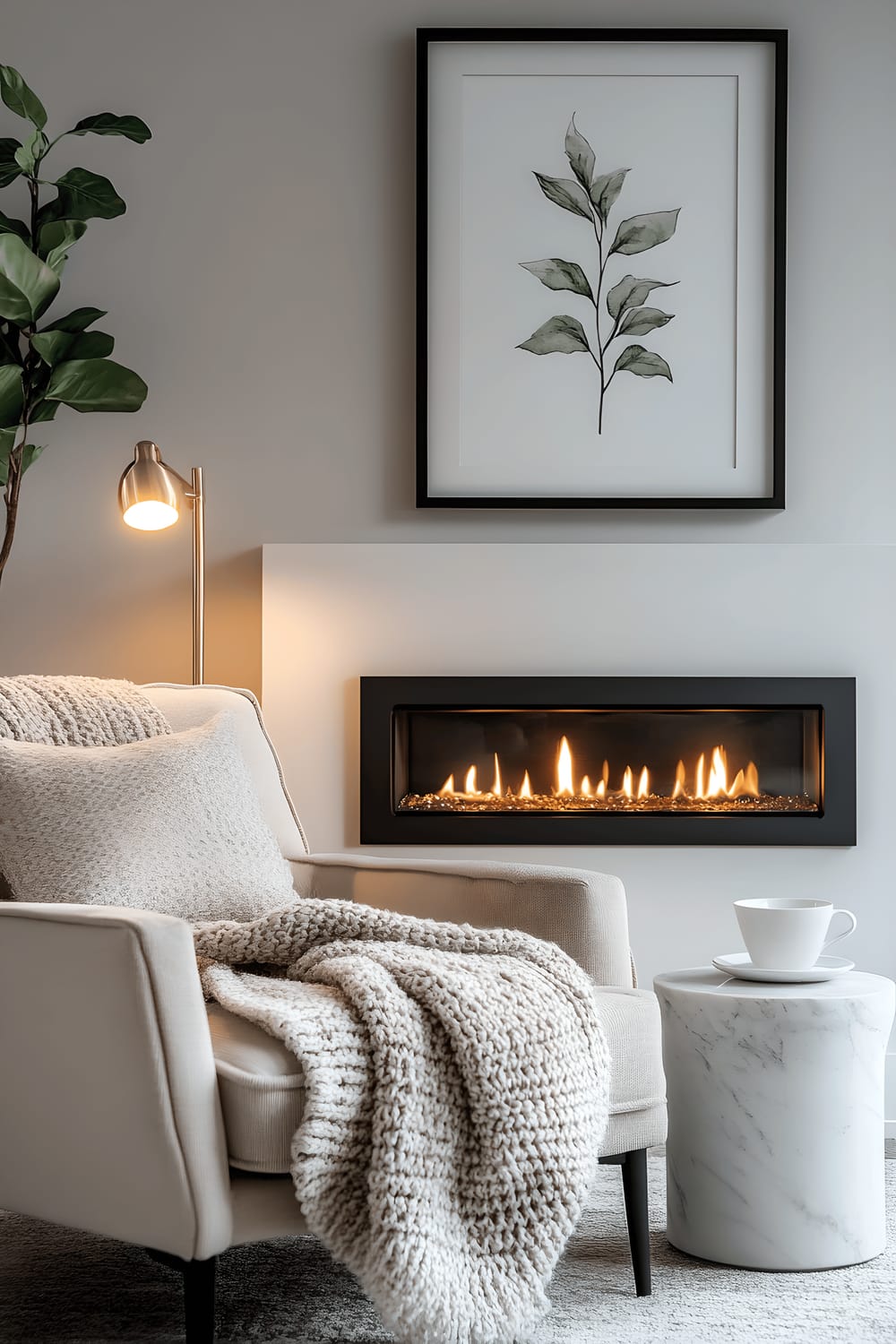 A cosy corner of the room featuring a modern linear gas fireplace with a matte black frame set into a light gray wall, above which hangs a large framed botanical illustration in soft green tones. Next to the fireplace, is a plush cream-colored velvet armchair with a chunky knit blanket on it and a small round marble side table with a delicate porcelain tea set on top. The area is tastefully lit with soft, ambient lighting from a nearby floor lamp with a linen shade. A tall, slender fiddle leaf fig in a matte white planter enhances the serene atmosphere of the setup.