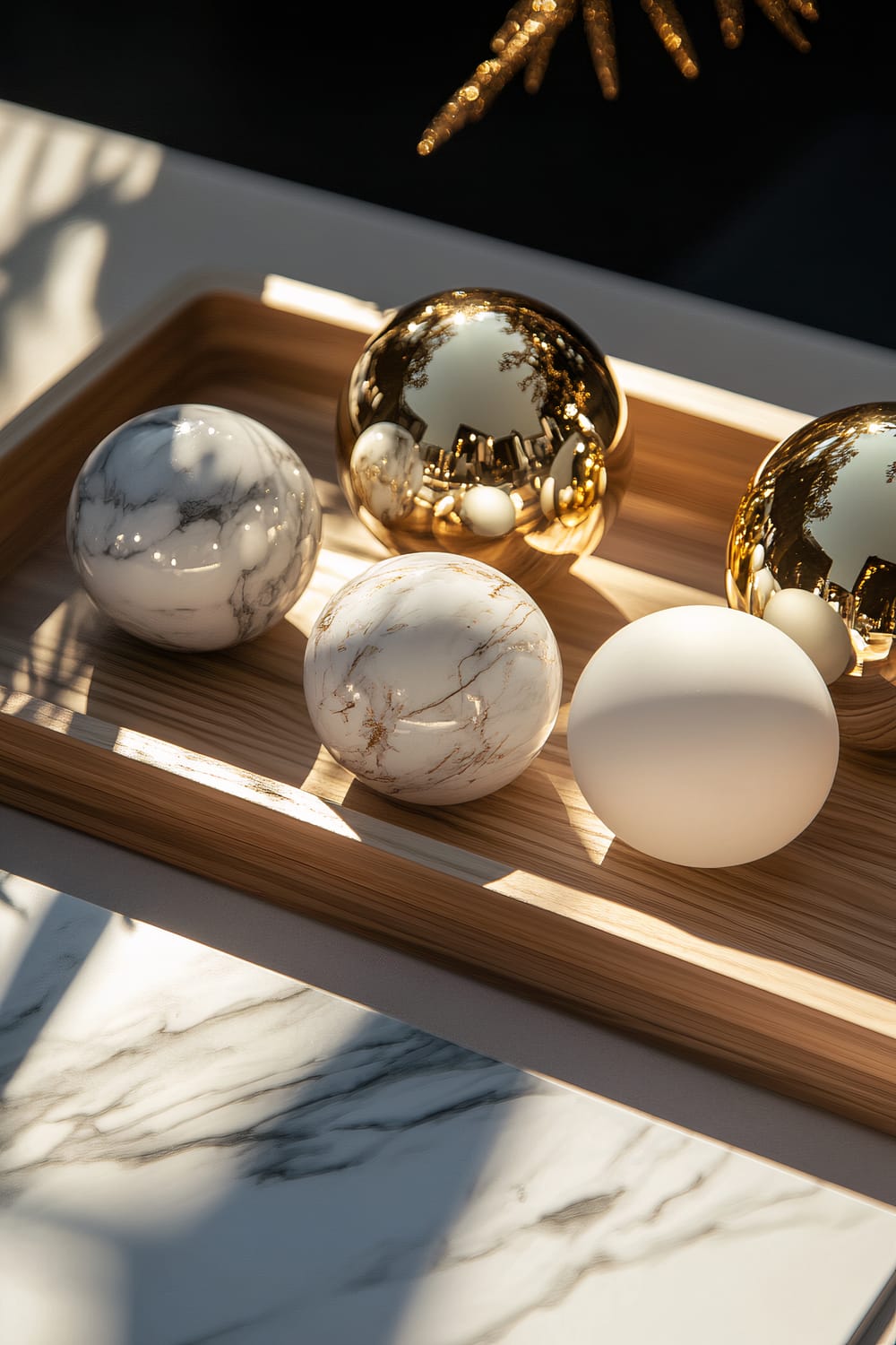 A sophisticated display featuring marble and gold spherical ornaments arranged on a minimalist wooden tray. The lighting creates striking highlights and deep shadows on the reflective surfaces.