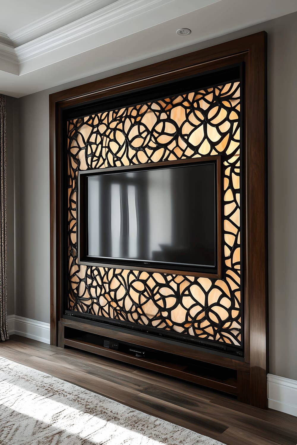 A television screen is set within a large, ornate frame made of stained glass, with intricate patterns in muted earth tones. The frame is mounted on a soft gray wall, illuminated by a gentle backlight that casts a glow around the stained glass without causing glare on the TV screen.